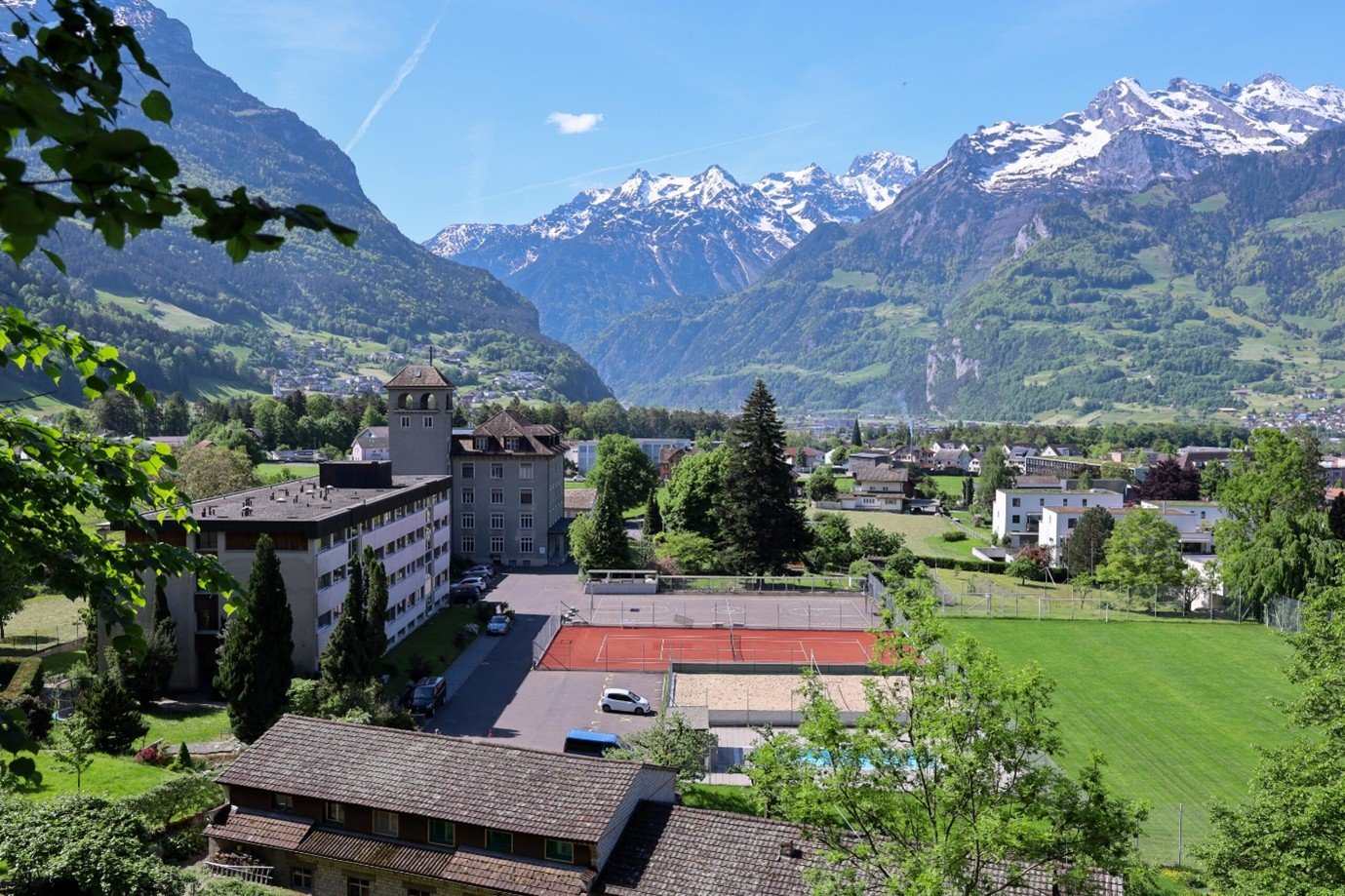 Overview of the ISSU campus with the school building, tennis court, football field and the snow-capped mountains of Uri
